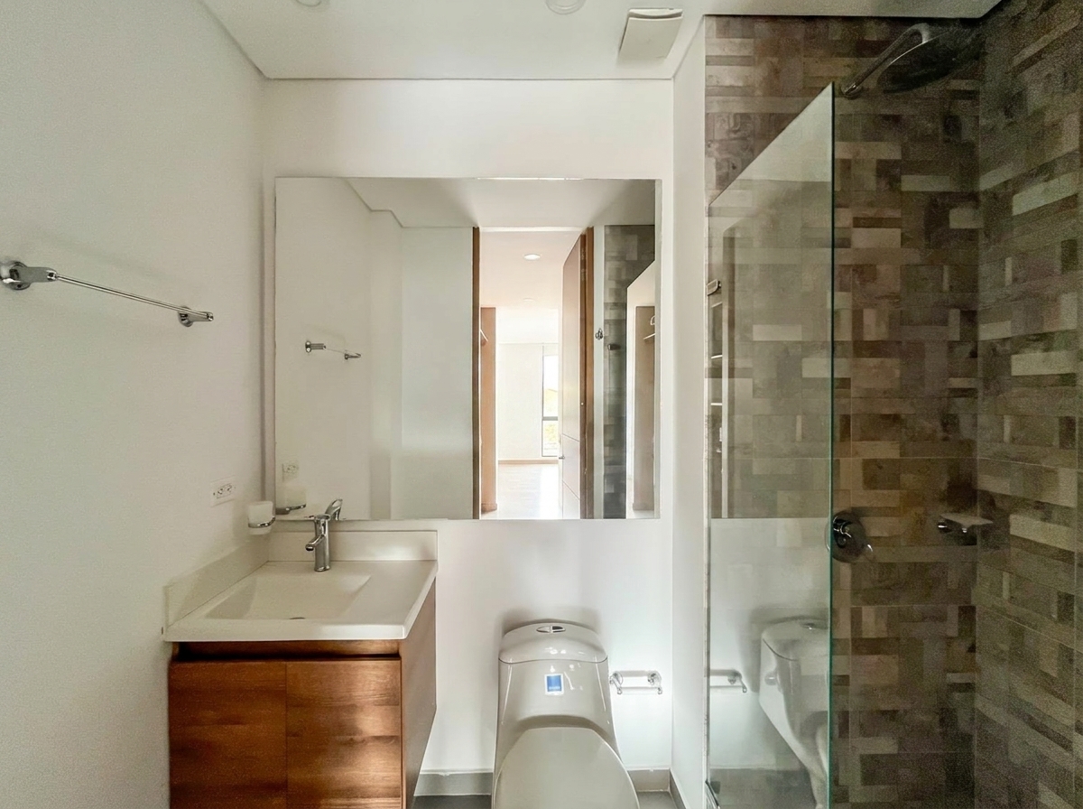 Baño con ducha en vidrio, muro en mosaico de piedra y mueble en madera