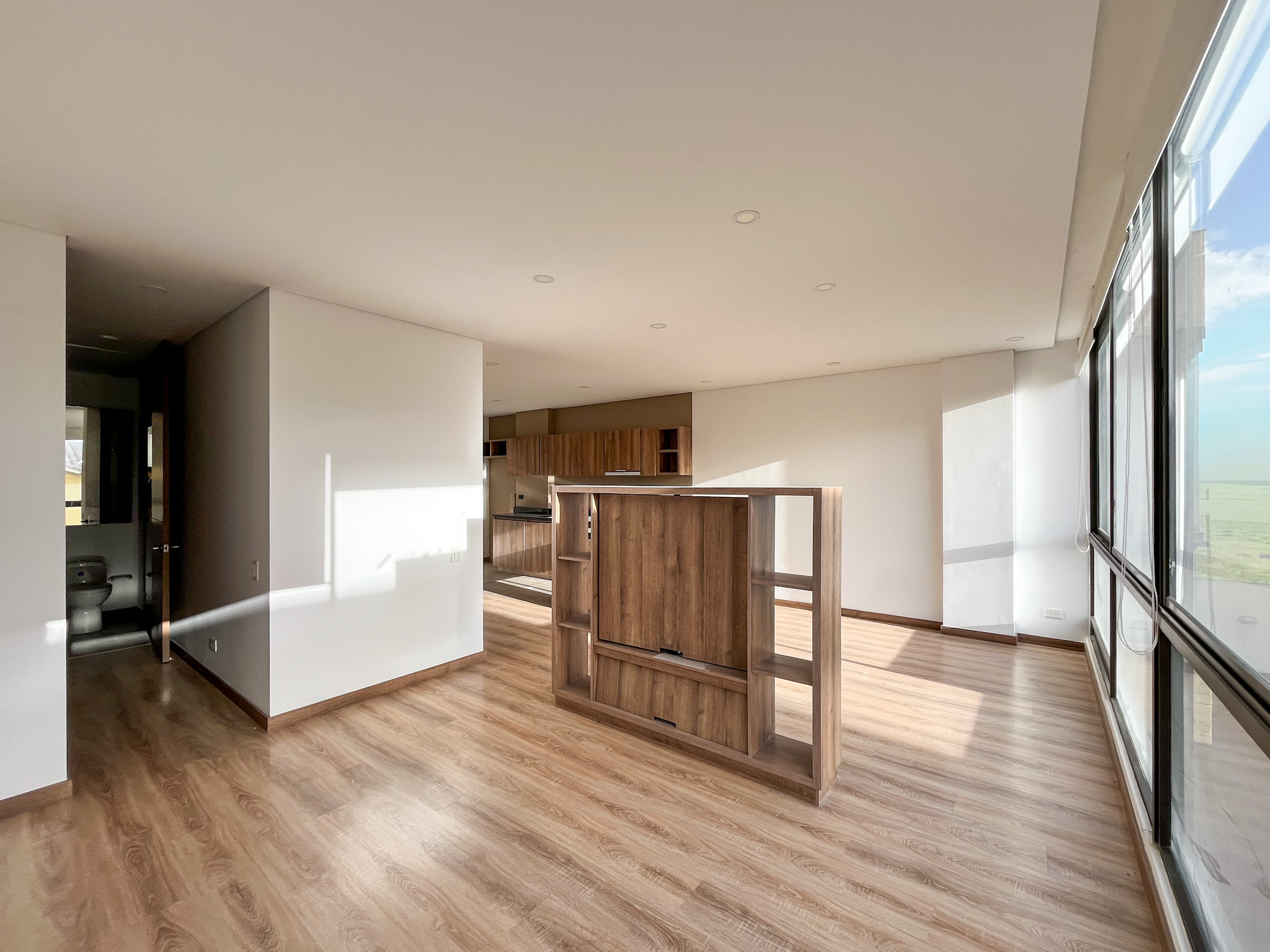 Sala del apartamento con ventanal de piso a techo y luz de la tarde sobre el piso en madera